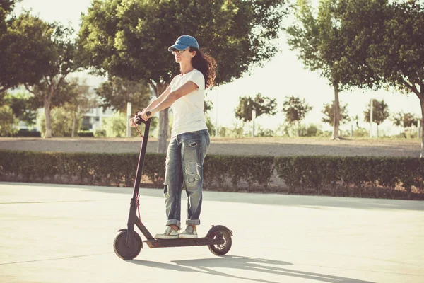 Woman, dressed in broken jeans, riding electric kick scooter — Stock Photo, Image