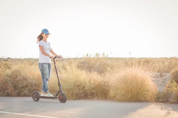 Kadın, çöl manzarasında, yolda elektrikli tekme scooter sürme