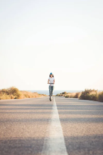 Yalnız bir yolda elektrikli tekme scooter sürme Kadın