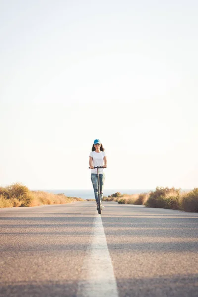 Yalnız bir yolda elektrikli tekme scooter sürme Kadın