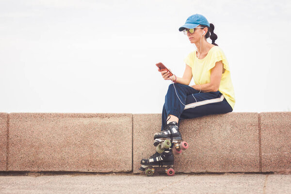 Woman with roller skates resting while looking at her mobile phone