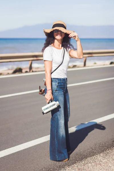 Film yapımcısı eski 8 mm 'lik film kamerasını elinde tutarken yolun kenarında sırıtarak bekliyor.