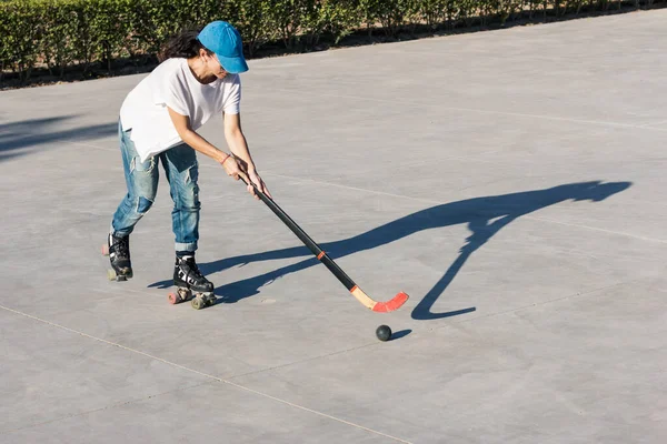 Girl playing roller hockey in the park. She wears a blue cap and jeans.