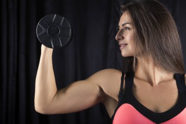 Karanlık bir arka plan üzerinde dumbbells ile poz kusursuz bir beden ile parlak spor formdaki güzel esmer