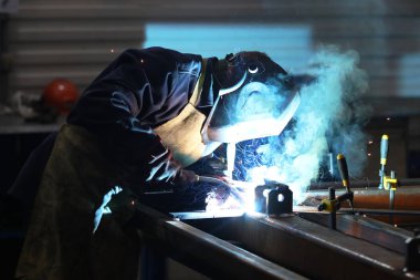 Koruyucu giysili ve maskeli bir adam demir parçaları kaynaklıyor.