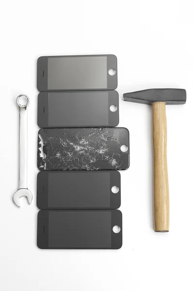 Large open-end wrench and a hammer lying near the broken screen and the new screens from the phone. Phone repair concept