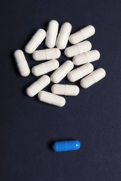 A bunch of white pills and one blue on a dark background