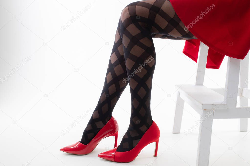 Feet of a girl in pantyhose with red shoes on a white background
