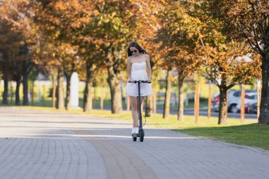 Bir kız güzel havalarda şehirde elektrikli scooterla gezer.
