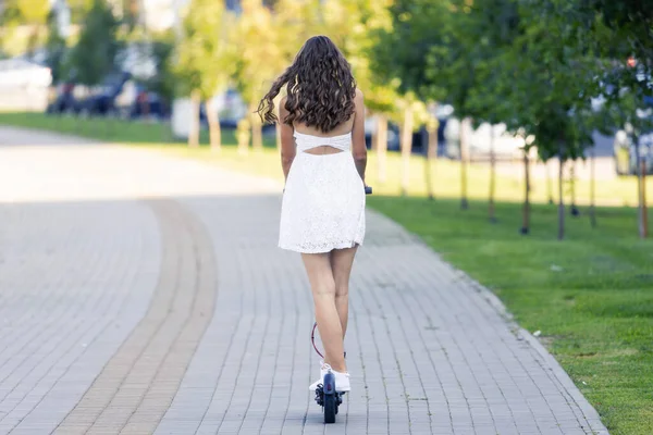 Bir kız güzel havalarda şehirde elektrikli scooterla gezer.