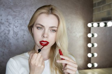 Bir kız, güzellik salonundaki aynanın önünde kırmızı dudaklarla parlak makyaj yapar..