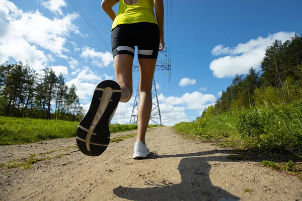 女性のランナーの足のクローズアップ 森に沿って街の外を走る — ストック写真