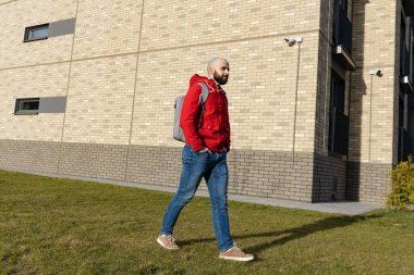 Sırt çantalı sıradan bir adam güneşli havada şehirde dolaşıyor.