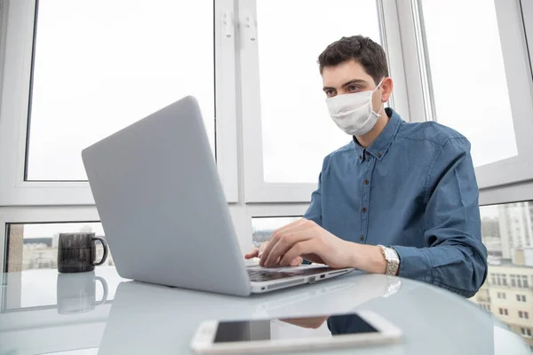 A guy in a protective face mask works at a computer from home during a virus epidemic. Quarantine during viral infection