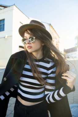 Montlu, gözlüklü ve şapkalı güzel bir esmer şehir manzaralarının arka planında poz veriyor. Sokak modası