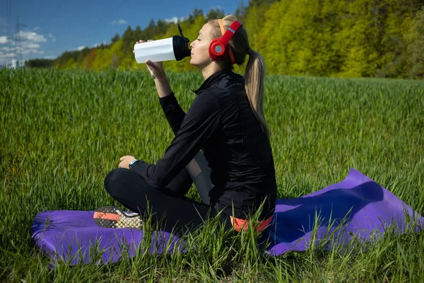 Una Chica Está Sentada Una Alfombra Fitness Escuchando Música Bebiendo — Foto de Stock