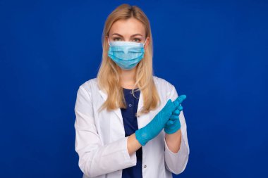 Mavi arka planda, tıbbi maskeli ve eldivenli bir doktor.