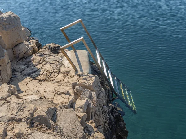 Paslanmaz çelik merdiven deniz kıyısında monte lider açık mavi denize kayalar.