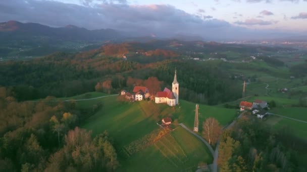 小さな丘の上に小さな教会周辺航空写真 飛んでいます 早朝の秋の美しいスロベニア国の風景を撮影 — ストック動画