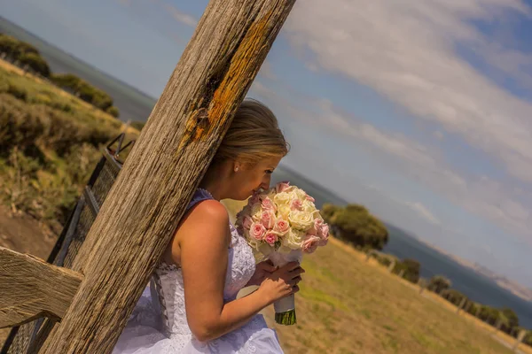 Ahşap çerçeve eğilerek çiçek buketi holding beyaz gelinlik içinde gelin. Avustralya inanılmaz kum plaj düğün ateş.