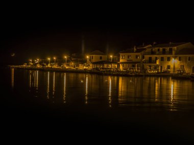 Deniz kıyısında ışıkları ve denizde geceleri yansıtan arka planda ay.