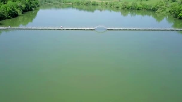 航空写真 は湖の反対側に浮体橋を渡ると小さな湖の上に飛んでいます 水から反射する太陽と美しい日当たりの良い夏の日 — ストック動画