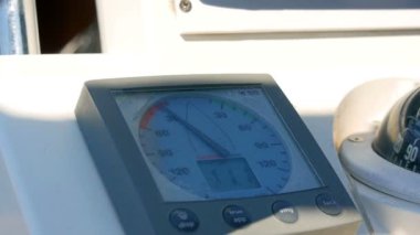 Sailing boats instrument by the steering wheel showing wind direction and speed. Closeup on windex and some rotating blurred steering wheel.