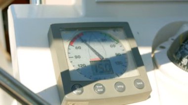 Sailing boats instrument by the steering wheel showing wind direction and speed. Closeup on windex and some rotating blurred steering wheel.