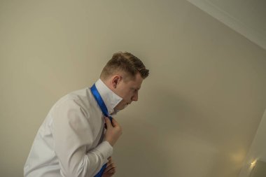 Aynanın önünde duran mavi kravat bağlama Beyaz tişörtlü adam.