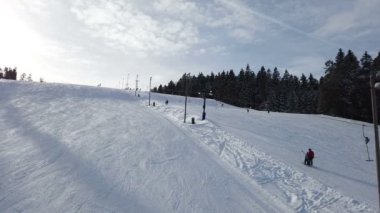 Rogla, Slovenya, 2019.01.29: Kayak pistinin yanındaki telesiyejden kayakçılarla manzara. Soğuk güneşli kış gününde güzel kayak merkezi filme.
