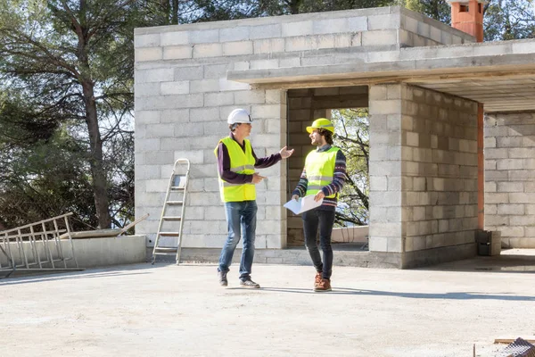 Discussion between a site manager and the architect during the construction site visit of a house under construction