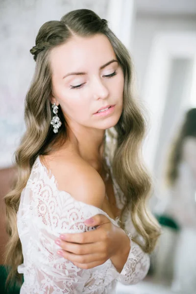 美丽的年轻新娘与长的金发卷发在一个白色的蕾丝睡衣在早晨在镜子 — 图库照片