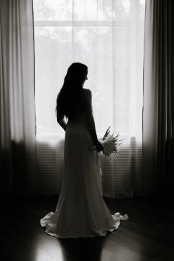 Uzun beyaz bir elbise ve bir buket pencereden uzun sarı kıvırcık saçlı güzel genç gelin