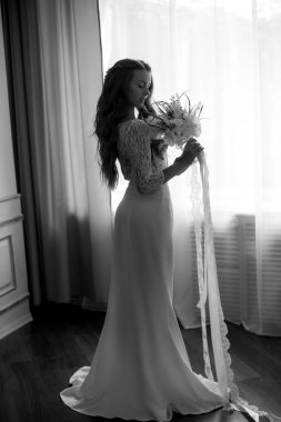 Uzun beyaz bir elbise ve bir buket pencereden uzun sarı kıvırcık saçlı güzel genç gelin