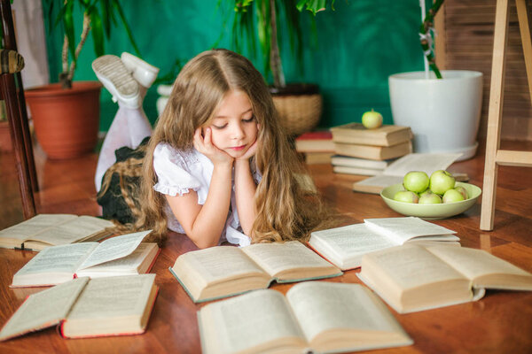 A sweet schoolgirl of junior classes with long blond hair with books, a school board and apples. School Fashion