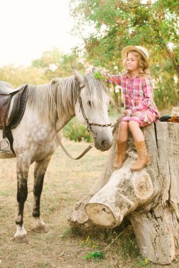 Vintage ekose elbise ve hasır şapka ve gri bir atı hafif kıvırcık saçlı tatlı bir küçük kız. Kırsal yaşam Güz. Atlar ve insanlar