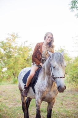 Bir süet ceket bir saçak gülümseyen ve günbatımı sonbaharda bir atı ata biner gibi uzun sarı saçlı güzel genç kız