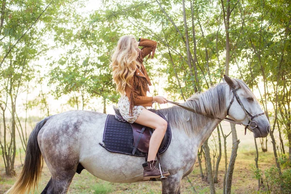 美丽的年轻女孩 长着金色的头发在一个麂皮绒夹克与条纹微笑 骑着马在秋季日落 — 图库照片