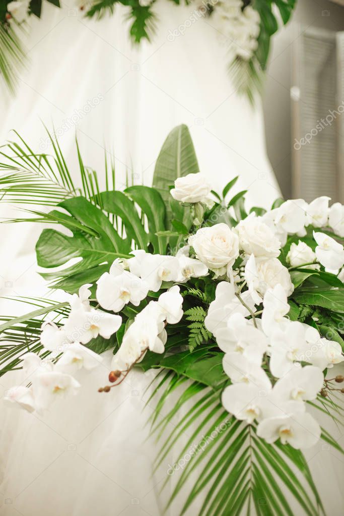 Elements of wedding decorations in a tropical style. Boudoir decorations with tropical leaves and white orchids, roses, feces and candles