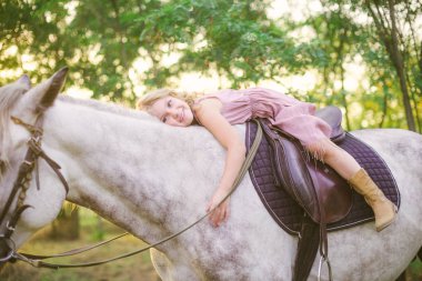 Hasır şapkalı bir binicilik bir güneşli sıcak sonbahar gün batımında hafif kıvırcık saçlı küçük şirin kız