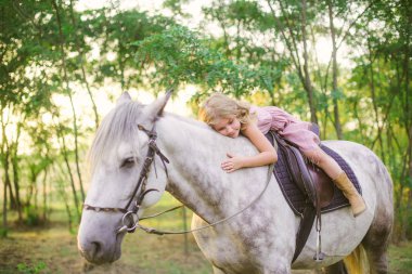 Hasır şapkalı bir binicilik bir güneşli sıcak sonbahar gün batımında hafif kıvırcık saçlı küçük şirin kız