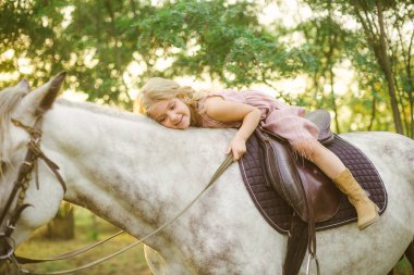 Hasır şapkalı bir binicilik bir güneşli sıcak sonbahar gün batımında hafif kıvırcık saçlı küçük şirin kız
