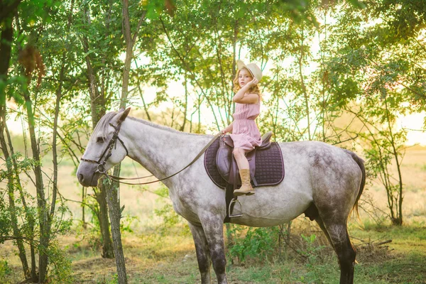 小可爱的女孩 在一个阳光明媚的秋日 在夕阳下骑着一匹马在一个草帽的卷发 — 图库照片