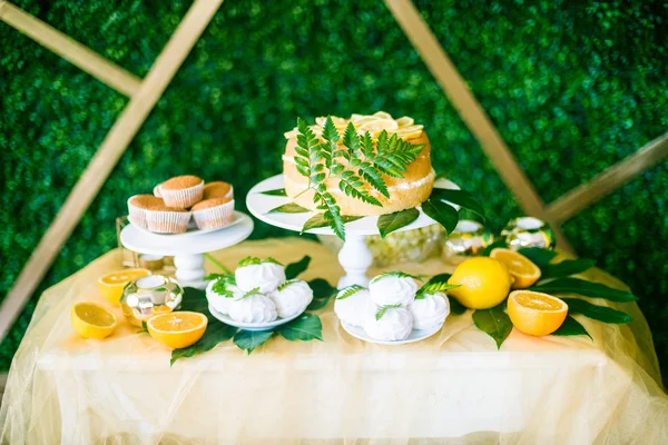 A festive kandi bar decorated in a tropical style with lemon cake muffins and marshmallows and bright balloons. Children\'s party in a tropical style with yellow, green and black balloons and tropical leaves