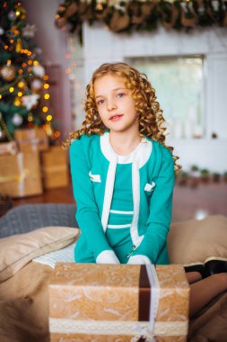 Kıvırcık saçlı sarışın evde hediyeler ve çelenk ve dekore edilmiş bir şömine ile Noel ağacı yakınındaki sevimli küçük kız 