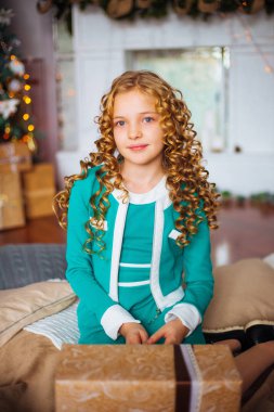 Kıvırcık saçlı sarışın evde hediyeler ve çelenk ve dekore edilmiş bir şömine ile Noel ağacı yakınındaki sevimli küçük kız 