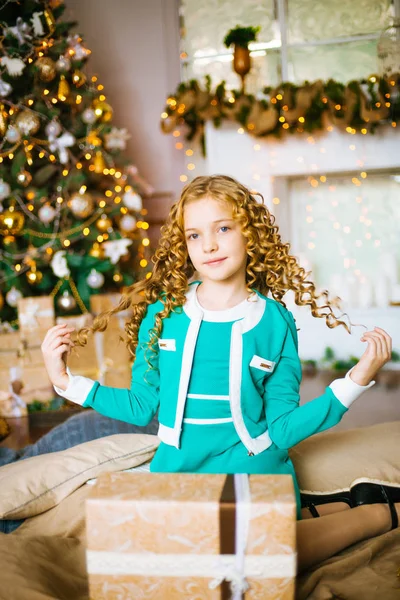 金髪巻き毛の家庭で装飾が施された暖炉と花輪ギフト クリスマス ツリー近くかわいい女の子 — ストック写真