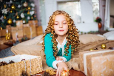 Kıvırcık saçlı sarışın evde hediyeler ve çelenk ve dekore edilmiş bir şömine ile Noel ağacı yakınındaki sevimli küçük kız 