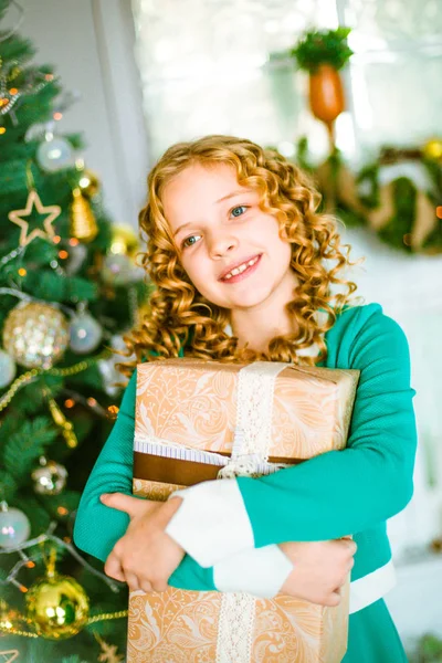 可爱的小女孩 金色卷发在家里附近的圣诞树与礼品和花环和装饰壁炉坐在格子和枕头 — 图库照片