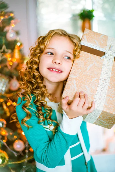 金髪巻き毛自宅ギフトと花輪と枕の上に座って装飾が施された暖炉とクリスマス ツリーの近くでかわいい女の子 — ストック写真